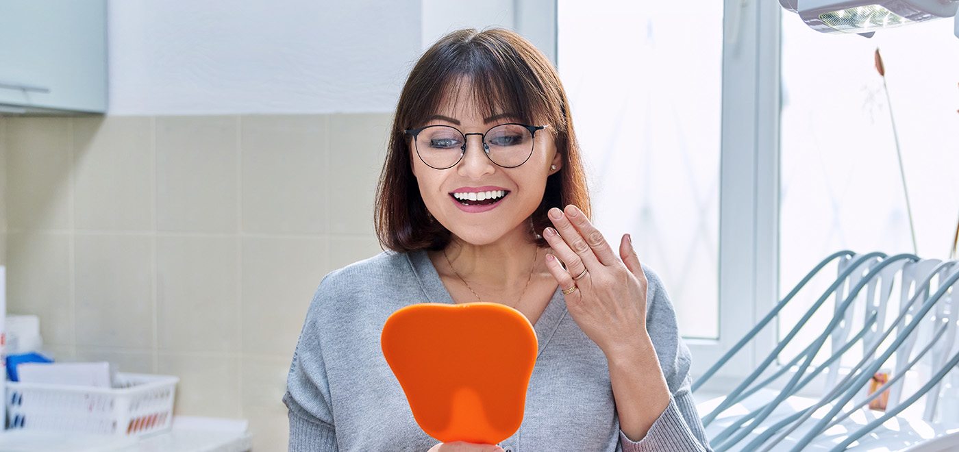Dental patient looking in mirror, admiring her new CEREC crown
