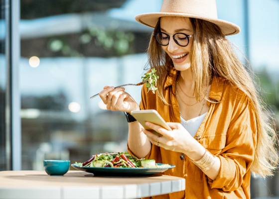 Smiling woman looking at her phone while eating a salad