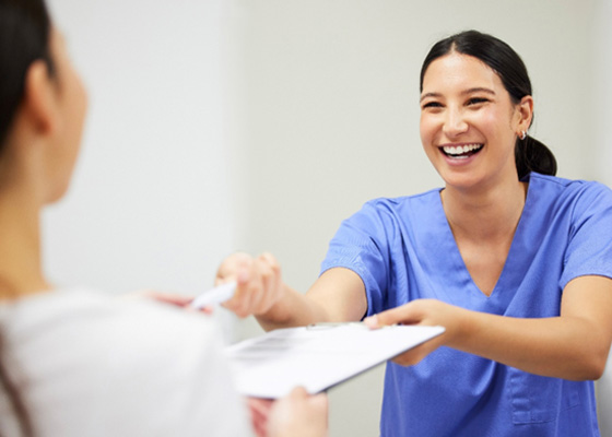 Smiling dental team member handing a clipboard to a patient