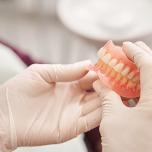 Technician carefully handling a freshly-finished set of dentures