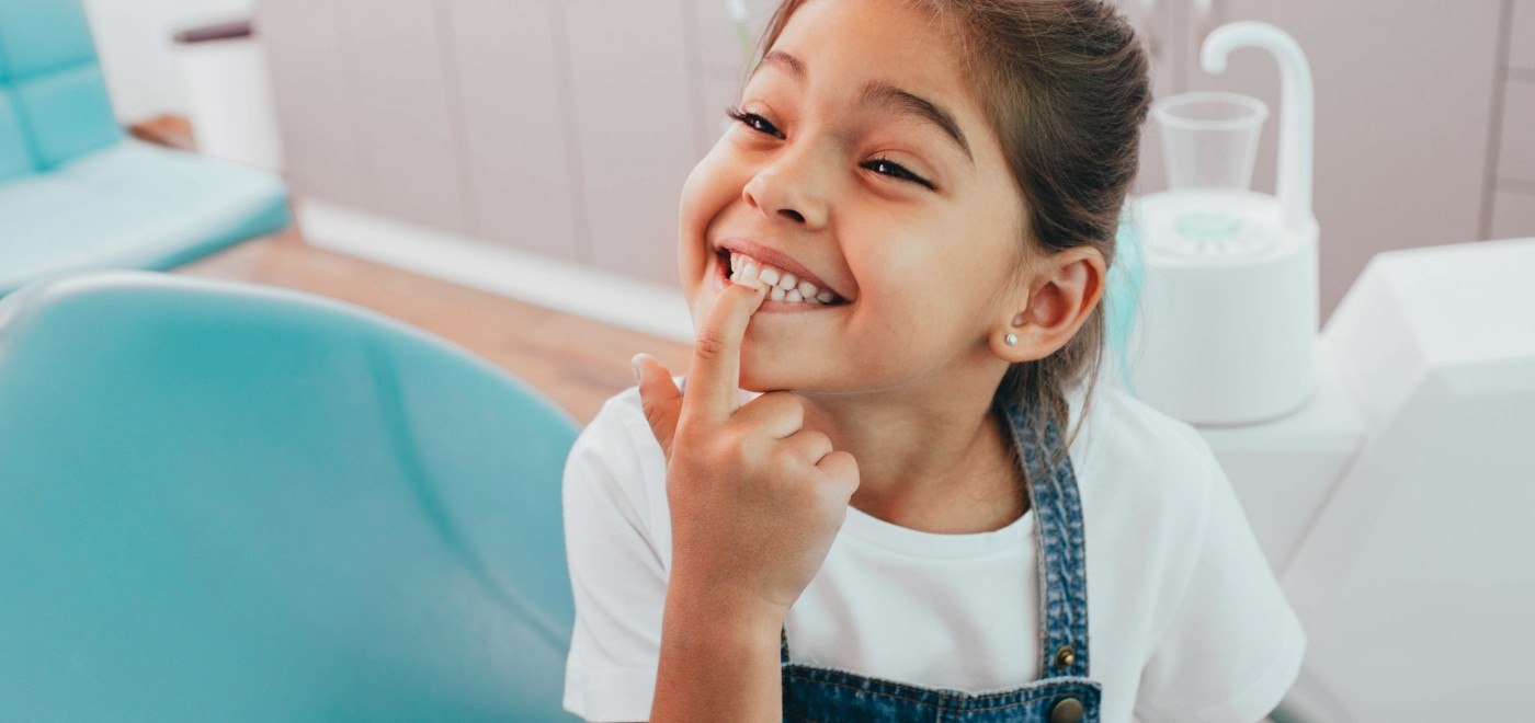 Smiling young girl in dental chair pointing to her teeth