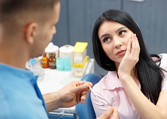 Woman holding face in pain looking at dentist about to examine her teeth
